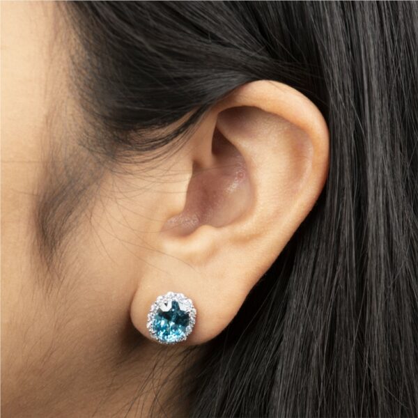 a woman's ear with a blue topazte and diamond earrings