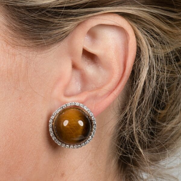a woman wearing a pair of earrings with a tiger's eye stone