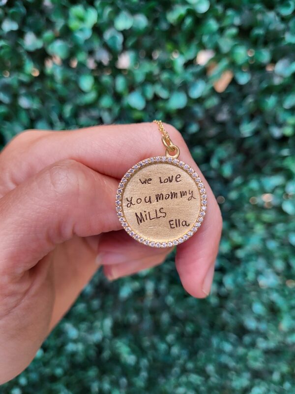 a person holding up a small round pendant with words on it